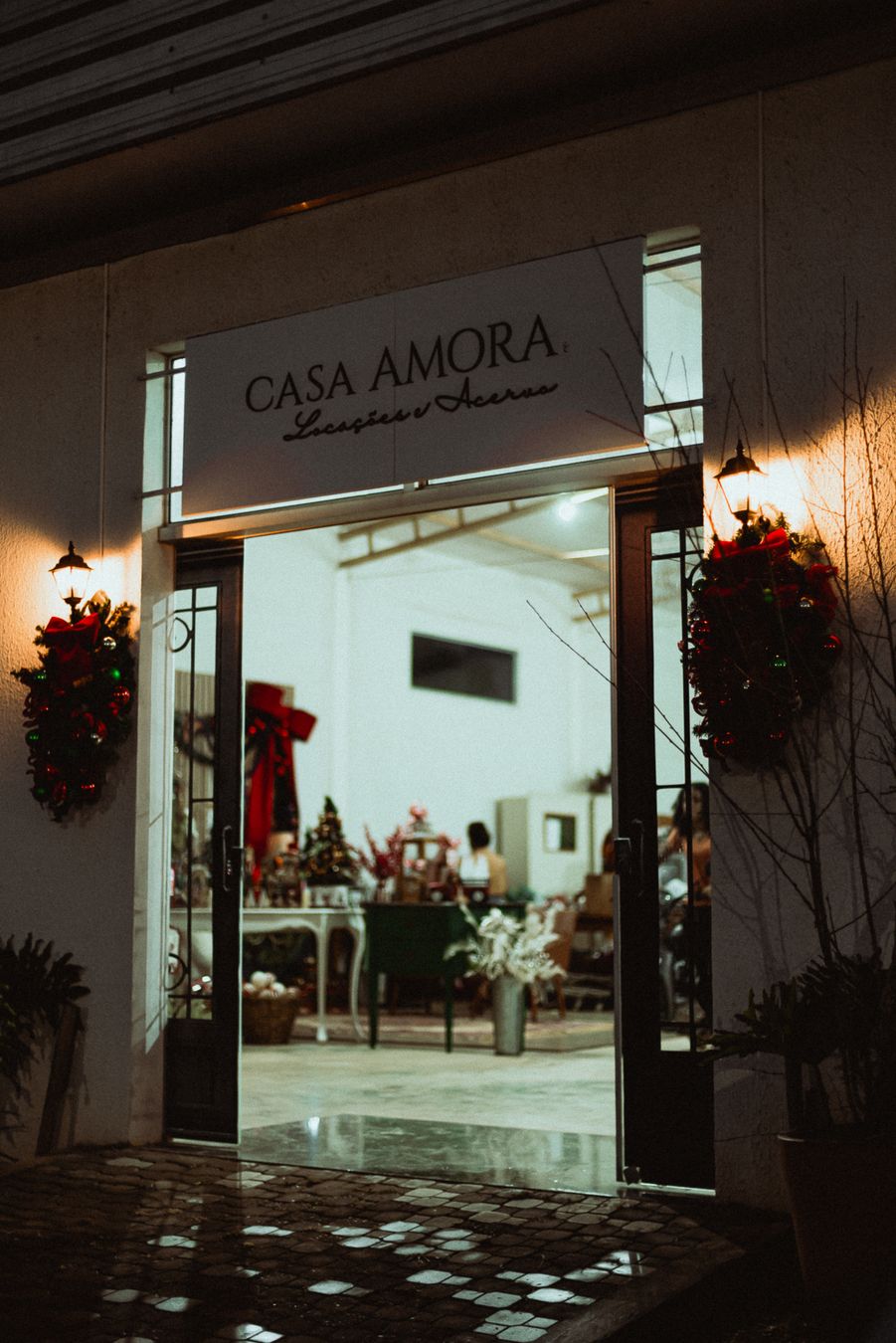 Fachada da Casa Amora Festas à noite, com guirlandas na porta